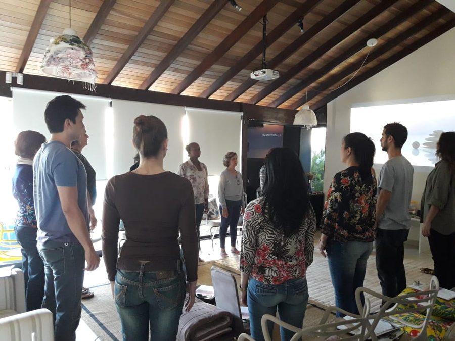 Um grupo de pé em roda, no salão de madeira aberto para o jardim